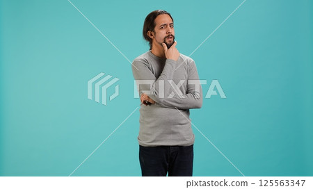 Pensive man deep in thoughts, doing ruminating hand gesturing, isolated over studio background. Unsure person doing stroking chin gesture, thinking, studio backdrop, camera A 125563347