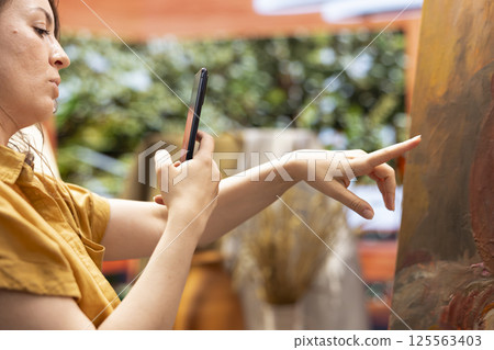 Woman artist recording a vlog to show her skill and painting techniques, creating a tutorial about inspiration in creating a rustic masterpiece. Painter does online painting lessons. 125563403