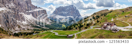 Majestic mountain panorama with winding road and snow-capped peaks in scenic landscape near Valley of Funes at Dolomites, Italy 125563433