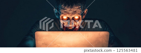 Undead man with glowing eyes working on a laptop in a dark, eerie room, embodying survival in a post apocalyptic world steeped in horror, decay, and danger 125563481