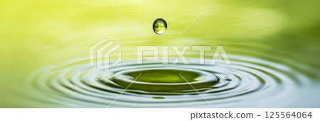 Single drop falling onto a green water surface, creating a mesmerizing circular ripple effect. Blurred shades of green and yellow in the background enhance the tranquil scene 125564064