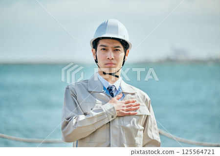 A young man in his 20s wearing work clothes with his hands on his chest 125564721