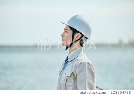 一位 20 多歲的年輕男子穿著工作服凝視遠方 125564728