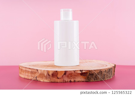 Cleaning agent, softener or liquid soap bottle on round wooden podium. Presentation of detergent mockup on pink background. Home sanitary liquid for laundry in plastic container 125565322