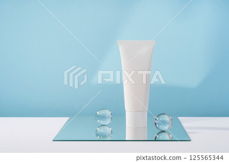 Unbranded cosmetic cream white plastic tube mockup on blue background with stylish props, mirror and glass balls. Body and health care beauty product packaging Unbranded cosmetic cream white plastic tube mockup on blue background with stylish props, mirror and glass balls. Body and health care beauty product packaging 125565344