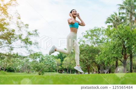 Young Asian woman in sportswear jumping happily during outdoor workout in a green park Young Asian woman in sportswear jumping happily during outdoor workout in a green park 125565484