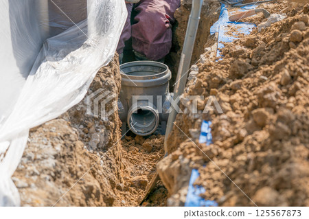 A worker installing a public sewage manhole during sewer piping work 125567873