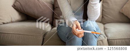 Anonymous woman holding pregnancy test sitting on couch at home Anonymous woman holding pregnancy test sitting on couch at home 125568808
