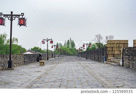 Scenic pathway along ancient city wall lined with traditional lanterns and lush greenery 125569535
