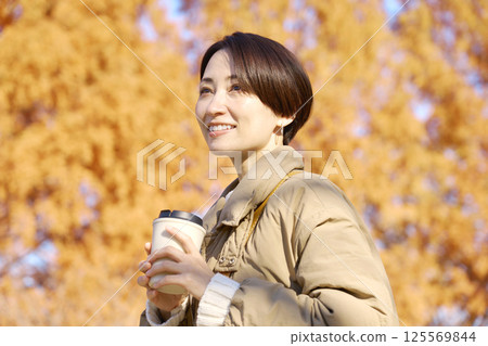 Middle-aged woman drinking coffee outdoors, autumn leaves Middle-aged woman drinking coffee outdoors, autumn leaves 125569844