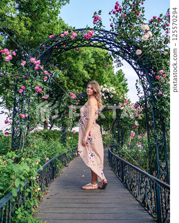 Young woman in floral dress walking through rose garden during golden hour 125570294