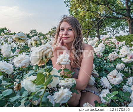 Young woman enjoying serenity among blooming white and pink roses in garden on sunny day 125570295