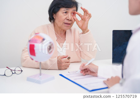 Elderly Patient consulting Doctor to Eye disease, Senior Medical Diagnosis. Anatomy Eye model for Cataract, Glaucoma, Age Related Macular Degeneration, Diabetic Retinopathy, Vitreous, health concept 125570719