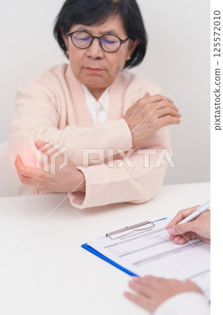Elderly Woman having elbow ache and consulting doctor in hospital. muscle pain due to lateral epicondylitis or tennis elbow. injury, Health and medical consultation concept 125572010