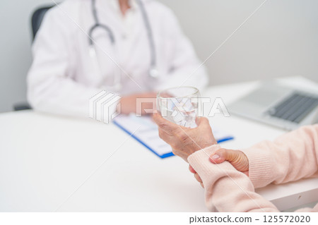 Senior woman with Tremor hand during taking glass of water in hospital. Parkinson disease April awareness month, Carpal Tunnel Syndrome, rheumatoid and brain injury and Neurological disorder concept 125572020