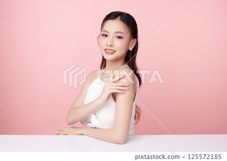 A beautiful young Asian woman with clean, fresh skin against a pink background. Skincare, facial treatment, cosmetology, beauty, and spa. An elegant portrait of an Asian woman. 125572185