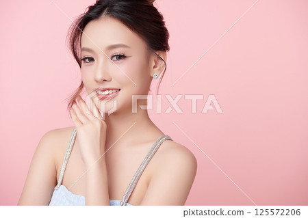 A beautiful young Asian woman with clean, fresh skin against a pink background. Skincare, facial treatment, cosmetology, beauty, and spa. An elegant portrait of an Asian woman. 125572206