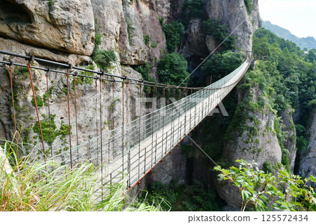 a suspension bridge on the edge of a cliff in the mountains, Zhejiang Province, China 125572434