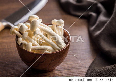 Raw white shimeji mushrooms in bowl on wooden table. Raw white shimeji mushrooms in bowl on wooden table. 125572512