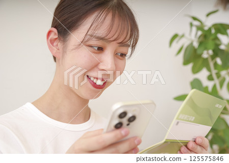 一位女士微笑著看著她的智慧型手機和存摺 一位女士微笑著看著她的智慧型手機和存摺 125575846