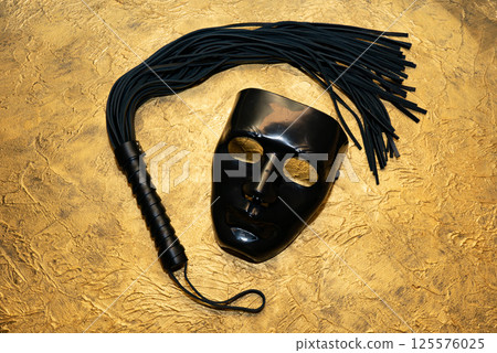 Adult sex games. Kinky lifestyle. Mask and whip ridding crop on the golden background. Bdsm outfit Adult sex games. Kinky lifestyle. Mask and whip ridding crop on the golden background. Bdsm outfit 125576025
