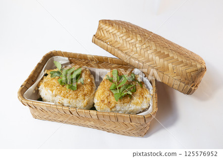白色背景的竹製午餐盒中放有味噌醬、芝麻和日本胡椒葉的烤飯糰的照片 白色背景的竹製午餐盒中放有味噌醬、芝麻和日本胡椒葉的烤飯糰的照片 125576952
