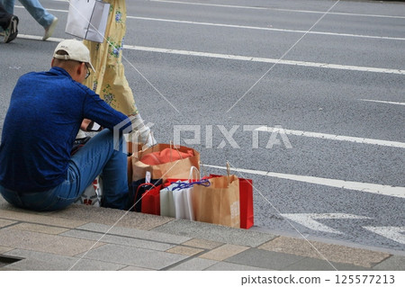 Shoppers sitting and resting on the sidewalk in a pedestrian zone 125577213