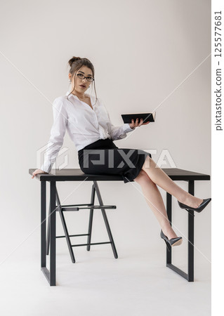 Businesswoman with glasses sitting on office table and holding black tablet Businesswoman with glasses sitting on office table and holding black tablet 125577681