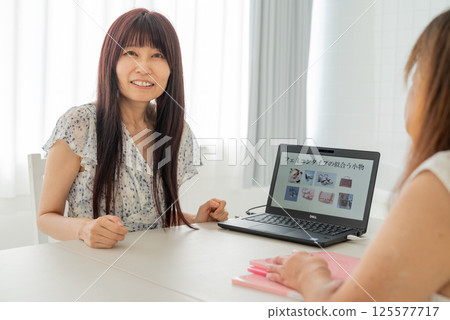 A middle-aged female advisor explaining things to a middle-aged woman using a laptop 125577717