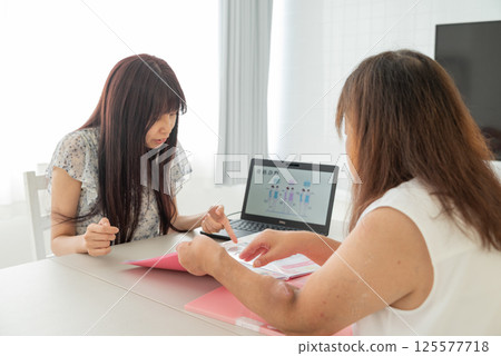 A middle-aged female advisor explaining things to a middle-aged woman using a laptop A middle-aged female advisor explaining things to a middle-aged woman using a laptop 125577718