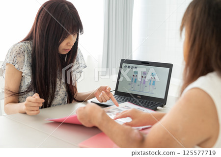 一位中年女性顧問正在用筆記型電腦向一位中年婦女講解 一位中年女性顧問正在用筆記型電腦向一位中年婦女講解 125577719