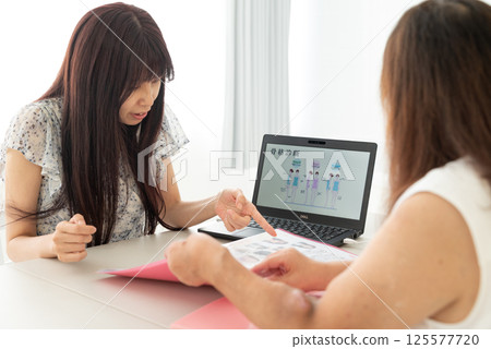 一位中年女性顧問正在用筆記型電腦向一位中年婦女講解 125577720