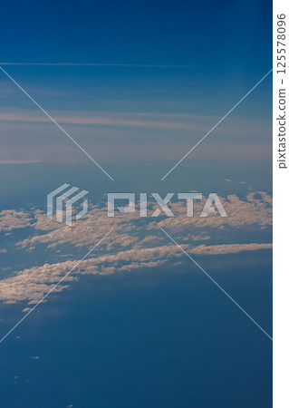 Aerial view from airplane window above green ground. View from the airplane window with beautiful clouds at sunrise. Earth and sky as seen through window of an airplane. 125578096