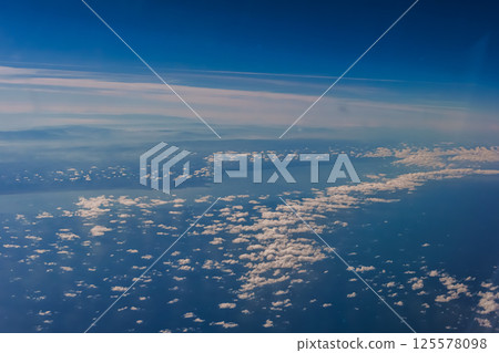 Aerial view from airplane window above green ground. View from the airplane window with beautiful clouds at sunrise. Earth and sky as seen through window of an airplane. Aerial view from airplane window above green ground. View from the airplane window with beautiful clouds at sunrise. Earth and sky as seen through window of an airplane. 125578098