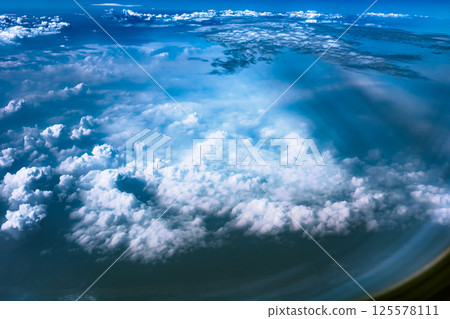 Aerial view from airplane window above green ground. View from the airplane window with beautiful clouds at sunrise. Earth and sky as seen through window of an airplane. 125578111