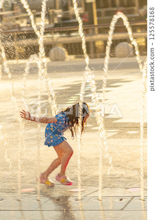 Adorable llittle girl playing with fountain on warm summer day. Child having fun with water on hot day. Outdoor summer activities for kids. High quality photo 125578168