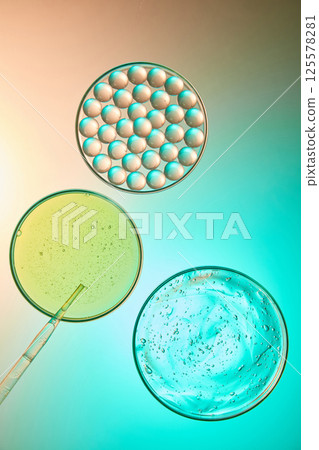 Biology concept with some laboratory dishes containing essence bubbles, yellow liquid and aloe vera gel. Bubbles are arranged side by side in a circular dish. Pink and blue gradient background. 125578281