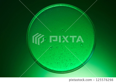 Petri dish is circular and contains a gel-like substance with a glistening surface, dotted with tiny air bubbles and a few larger bubbles. Chemical laboratory research with gradient green background. Petri dish is circular and contains a gel-like substance with a glistening surface, dotted with tiny air bubbles and a few larger bubbles. Chemical laboratory research with gradient green background. 125578298