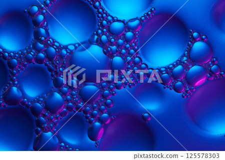Macro of tiny transparent bubbles crowding the spaces between larger bubbles. The molecular surface is glossy, reflecting blue and purple light at different angles. Abstract cosmetic laboratory.  125578303