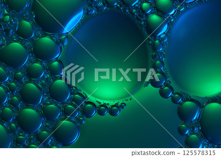 The essence drops onto the neon green background, forming two large bubbles, surrounded by countless other tiny bubbles clinging to the edges. Close-up of molecules in a cosmetic essence.  125578315