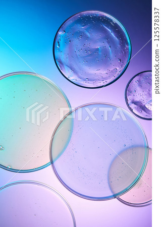 Vertical photo of round plates used in the experiment stacked on a background of blue, purple and white liquid. The cosmetic essence has thick texture and numerous air bubbles floating on top. Vertical photo of round plates used in the experiment stacked on a background of blue, purple and white liquid. The cosmetic essence has thick texture and numerous air bubbles floating on top. 125578337
