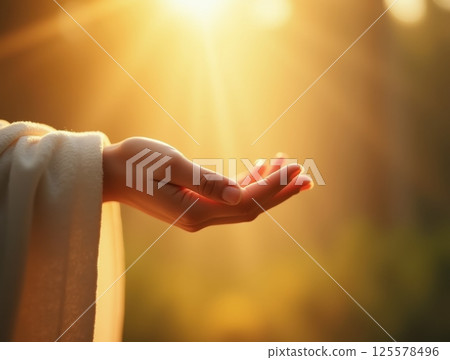 Outstretched hand in white robe reaching toward golden sunlight, symbolizing faith and hope. 125578496