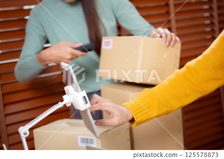 Closeup hand woman live online while scanning package with barcode reader in office. Closeup hand woman live online while scanning package with barcode reader in office. 125578873