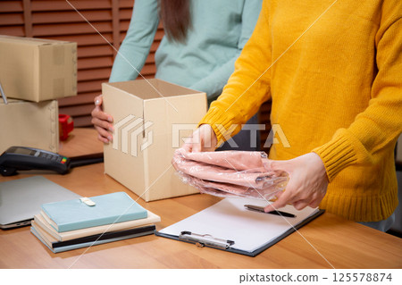 Closeup hand of woman packing in cardboard box for shipping or storage in home office. 125578874