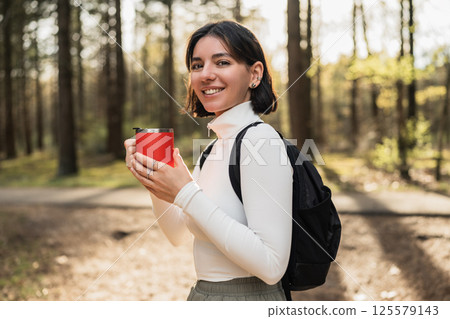 Woman hiker in casual gear sipping from a thermo mug in a peaceful forest, merging travel lifestyle with wellness vibes Woman hiker in casual gear sipping from a thermo mug in a peaceful forest, merging travel lifestyle with wellness vibes 125579143