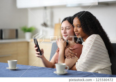 Interracial lesbian couple in the kitchen using phone Interracial lesbian couple in the kitchen using phone 125580472