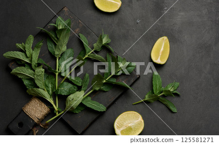 Whole and cut limes with fresh mint leaves arranged on a dark textured surface. Whole and cut limes with fresh mint leaves arranged on a dark textured surface. 125581271