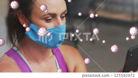Checking adult woman wearing blue cloth mask scrolling smartphone in gym Checking adult woman wearing blue cloth mask scrolling smartphone in gym 125582072