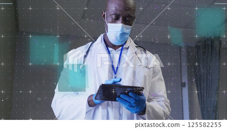 Image of data processing over male african american doctor wearing face mask using tablet 125582255