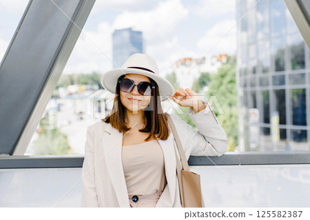 Beautiful brunette businesswoman wearing suit and white hat, walking on the street. Beautiful brunette businesswoman wearing suit and white hat, walking on the street. 125582387